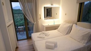 A bedroom with two beds, a bedside table with a lamp, a mirror, and a view of a natural landscape through a sliding door. - Terra Divina Damnoni (Agios Vasileios)