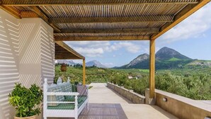 A covered outdoor seating area with a bench and potted plants, overlooking a mountainous landscape. - Terra Divina Damnoni (Agios Vasileios)