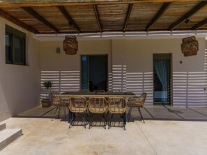 A covered patio with a table and chairs, a potted plant, and a view of the interior through a doorway.