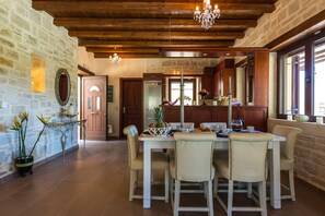 A dining area with a stone wall, wooden ceiling, and a chandelier. - Villa Poseidon Lefkogis (Agios Vasileios)