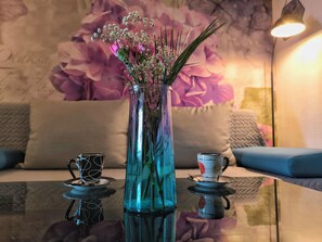 Um vaso de vidro com flores sobre uma superfície refletora, uma xícara de café e um castiçal.