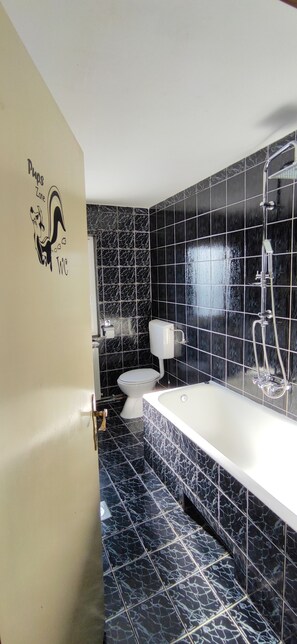 Casa de banho com sanita branca, banheira com chuveiro e mosaicos de mármore preto.
