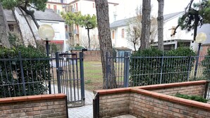 An outdoor seating area with a brick wall and metal fence, surrounded by trees and buildings. - Domus Lido - 3 Bedrooms, 5 Persons, Wifi, Parking, air Conditioning (Comacchio)