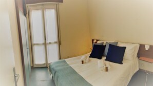 A hotel room with a bed, pillows, a towel, a bedside table, and a wardrobe. - Domus Lido - 3 Bedrooms, 5 Persons, Wifi, Parking, air Conditioning (Comacchio)