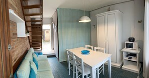 A compact room with a wooden loft bed, a white table with chairs, a blue bowl, a white cabinet with a microwave, and a small shelf with a radio. - Domus Lido - 3 Bedrooms, 5 Persons, Wifi, Parking, air Conditioning (Comacchio)