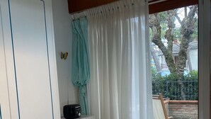 A room with a white table, a blue bowl, a microwave, a small table with a bottle, and a window with curtains. - Domus Lido - 3 Bedrooms, 5 Persons, Wifi, Parking, air Conditioning (Comacchio)