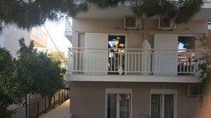 Un edificio de dos pisos con balcón, unidades de aire acondicionado y entrada protegida por un portón.