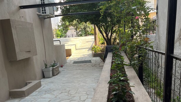 Un patio empedrado con un macizo de flores, una planta en maceta y una barandilla de metal.