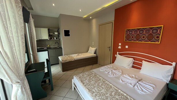 A hotel room with a bed, a desk, a chair, a small kitchenette, and a bathroom.