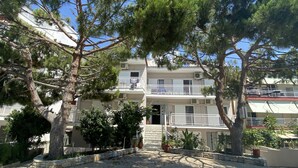 A multi-story building with balconies, stone steps leading to the entrance, and surrounding trees.