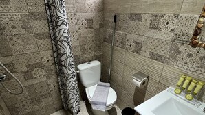 A bathroom with patterned tiles, a toilet, a shower, a sink, and a window.