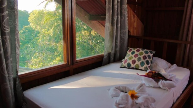 A single bed with a white sheet, a polka-dotted pillow, and a towel with a flower. - Triple Room With sea and Mountain Views Perfecto for Couples (Drake Bay)