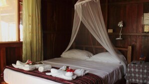 Una cama con estructura de madera y dosel, impecablemente tendida con toallas y una colcha a rayas rojas.