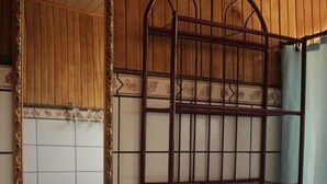 A bathroom with a wooden wall, a white sink with a mirror, a metal shelf, and a toilet.