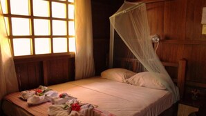 A single bed with a canopy, a bedside table with a lamp, and a window with curtains.