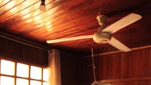 A wooden room with a bed, a ceiling fan, and a window with curtains.