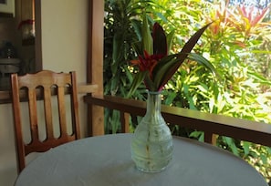 A clear view of a table with a glass vase containing a plant, a wooden chair, and a wooden railing.