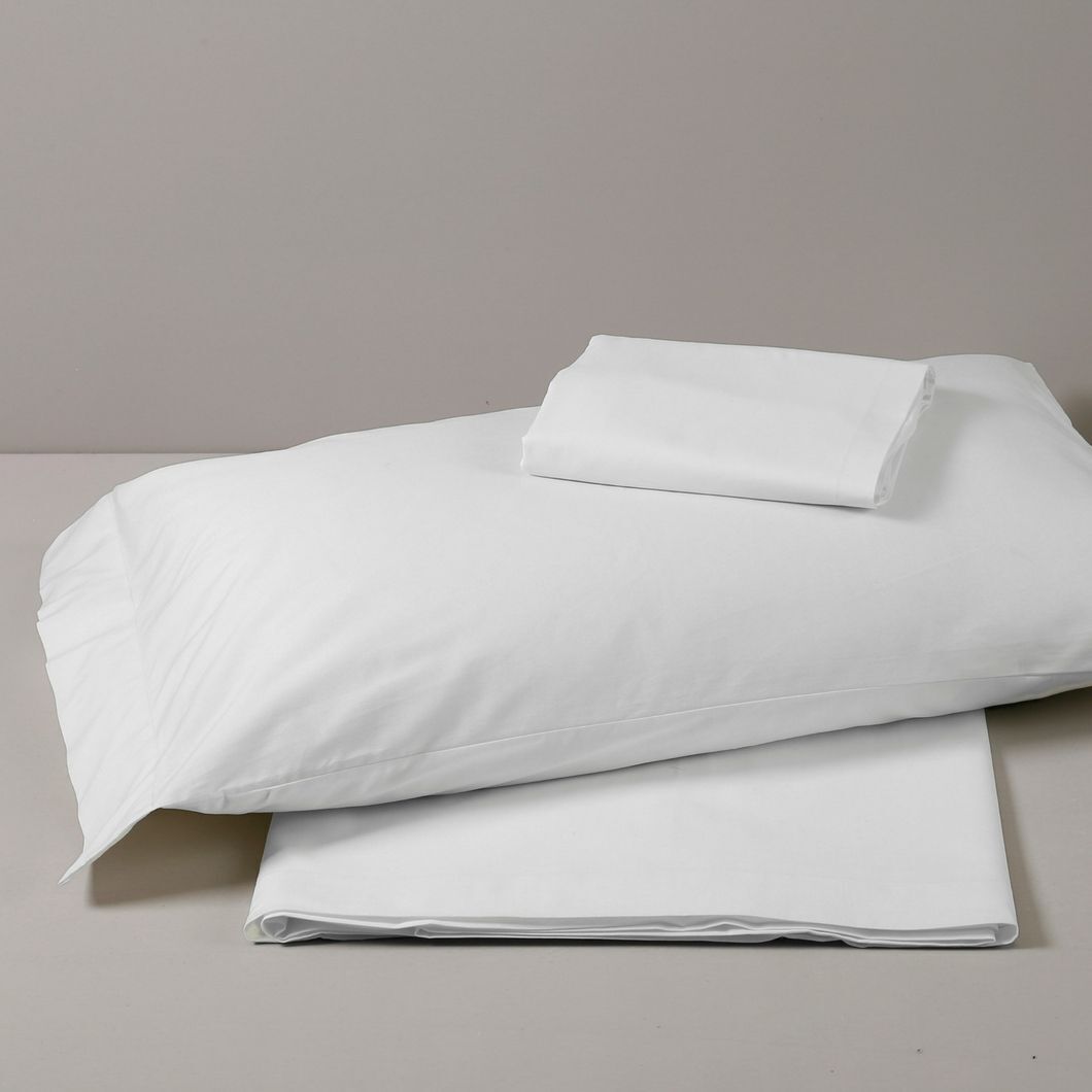 A neatly folded white bedspread and pillow on a plain surface.