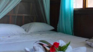 Una cama con mosquitero, almohadas blancas y una flor roja sobre la cama.