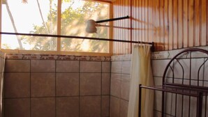 Un baño con pared de azulejos, un estante metálico y una ventana con cortina.
