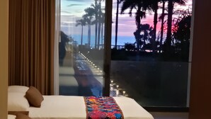 A hotel room with two beds, a large window with a view of the beach and palm trees, and a colorful bedspread. - Aria Ocean 208 Beach Front Apartment Nuevo Vallarta (Nuevo Nayarit)