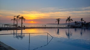 A pool with a sunset view, palm trees, and a distant mountain range. - Aria Ocean 208 Beach Front Apartment Nuevo Vallarta (Nuevo Nayarit)