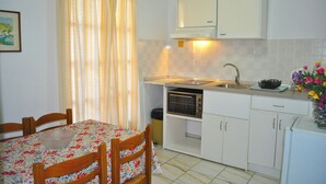 Een compacte keuken met een tafel, stoelen, een spoelbak, een fornuis en kastjes.