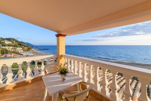 Un balcon avec une table et des chaises, donnant sur une plage et la mer.