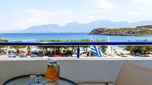 A balcony with a view of the sea and mountains, a table with a pitcher of drink, and outdoor seating with umbrellas. - Level Up Your Holidays in Crete (Agios Nikolaos)