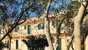 A courtyard with trees, a fence, and a building with balconies and windows. - Room-banos Apartments and Swimming Pool (Corfu)
