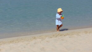 A person in a white robe and yellow hat standing on a sandy beach near the water. - Holiday Studio Kontogialos in Pelekas Beach, Corfu (Corfu)