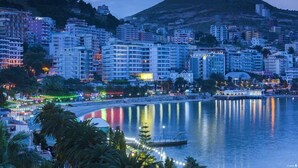 Eine Küstenstadt mit Hochhäusern, einem Yachthafen und ruhigem Wasser, das Lichter spiegelt.