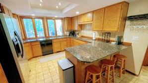 A kitchen with wooden cabinets, a granite countertop, a built-in oven, a refrigerator, and a small island with stools.