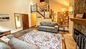 A spacious living room with a grey sofa, a patterned rug, a fireplace, and a staircase leading to an upper level.