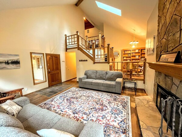 A spacious living room with a grey sofa, a patterned rug, a fireplace, and a staircase leading to an upper level.