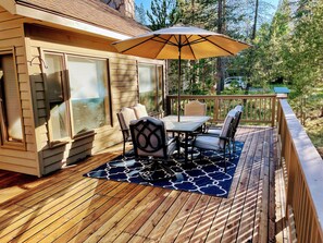 A wooden deck with a table and chairs, an umbrella, and a view of trees.