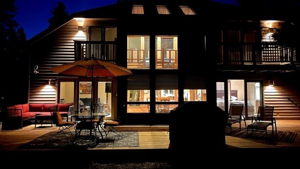 A two-story house with a patio area featuring a dining table and chairs, and a red sofa.