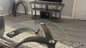 Ein Wohnzimmer mit Glastisch, Fernseher auf Holzfuß und einem gemusterten Teppich.