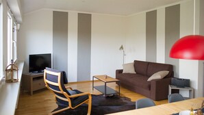 Ett modernt vardagsrum med en brun soffa, en trästol, en tv, ett litet bord och en röd hänglampa.