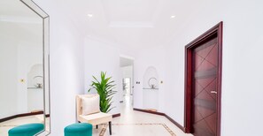 A hallway with a wooden door, a mirror, a chair, a plant, and a glass shelf. - LUX | The Ocean Pearl Villa (Dubai)