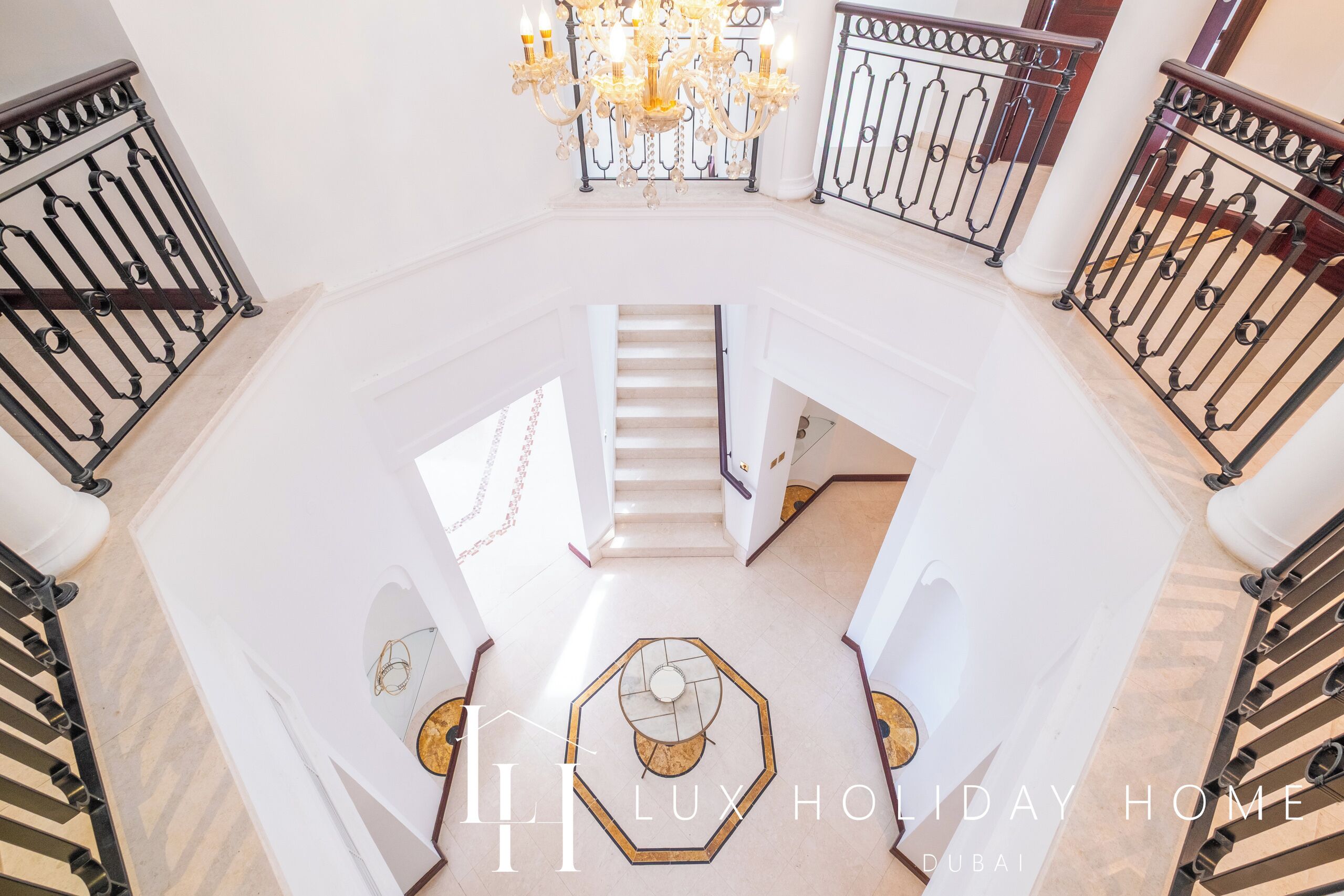 A spacious, well-lit foyer with a grand staircase, ornate metal railings, and a chandelier.