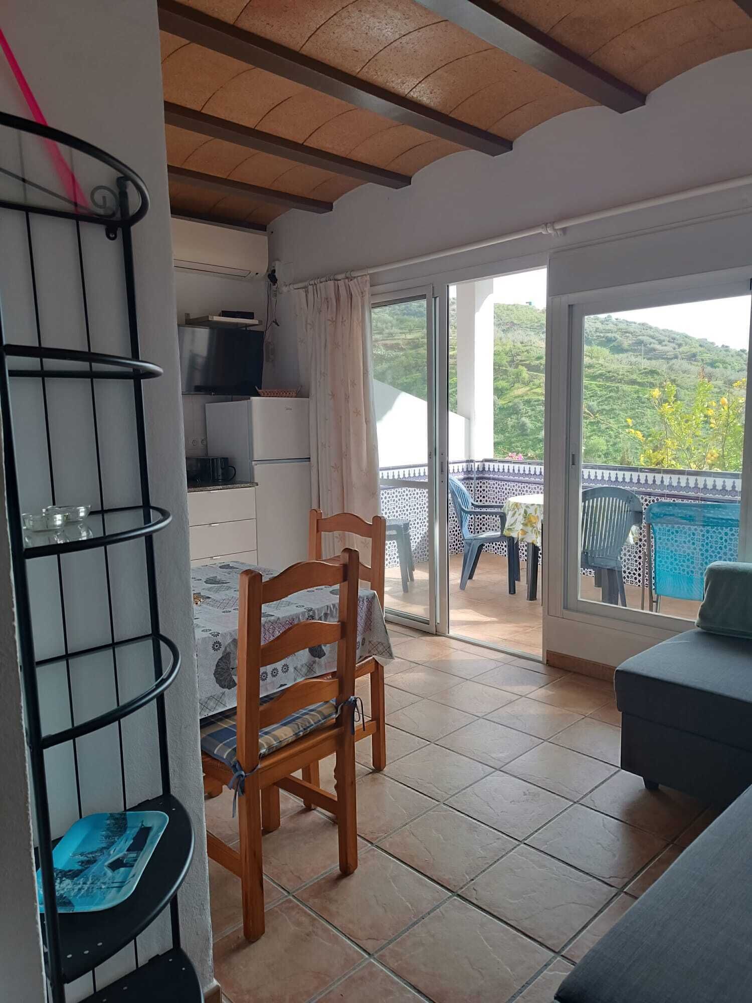 Une pièce avec une chaise en bois, une petite table, un téléviseur et un balcon donnant sur un paysage verdoyant.
