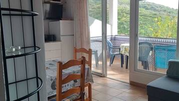 Une pièce avec une chaise en bois, une petite table, un téléviseur et un balcon donnant sur un paysage verdoyant.