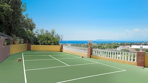 Un court de tennis offrant une vue sur la mer et les montagnes.