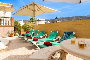 A terrace with lounge chairs, a table with drinks, and a view of mountains.