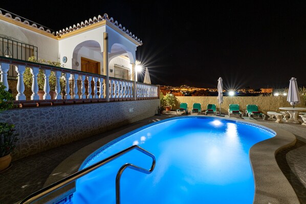 A swimming pool with a metal ladder, surrounded by a stone wall and a white fence with balusters.
