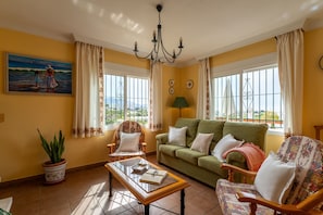 A living room with a green sofa, a wooden coffee table, a patterned armchair, and a painting of a beach scene.