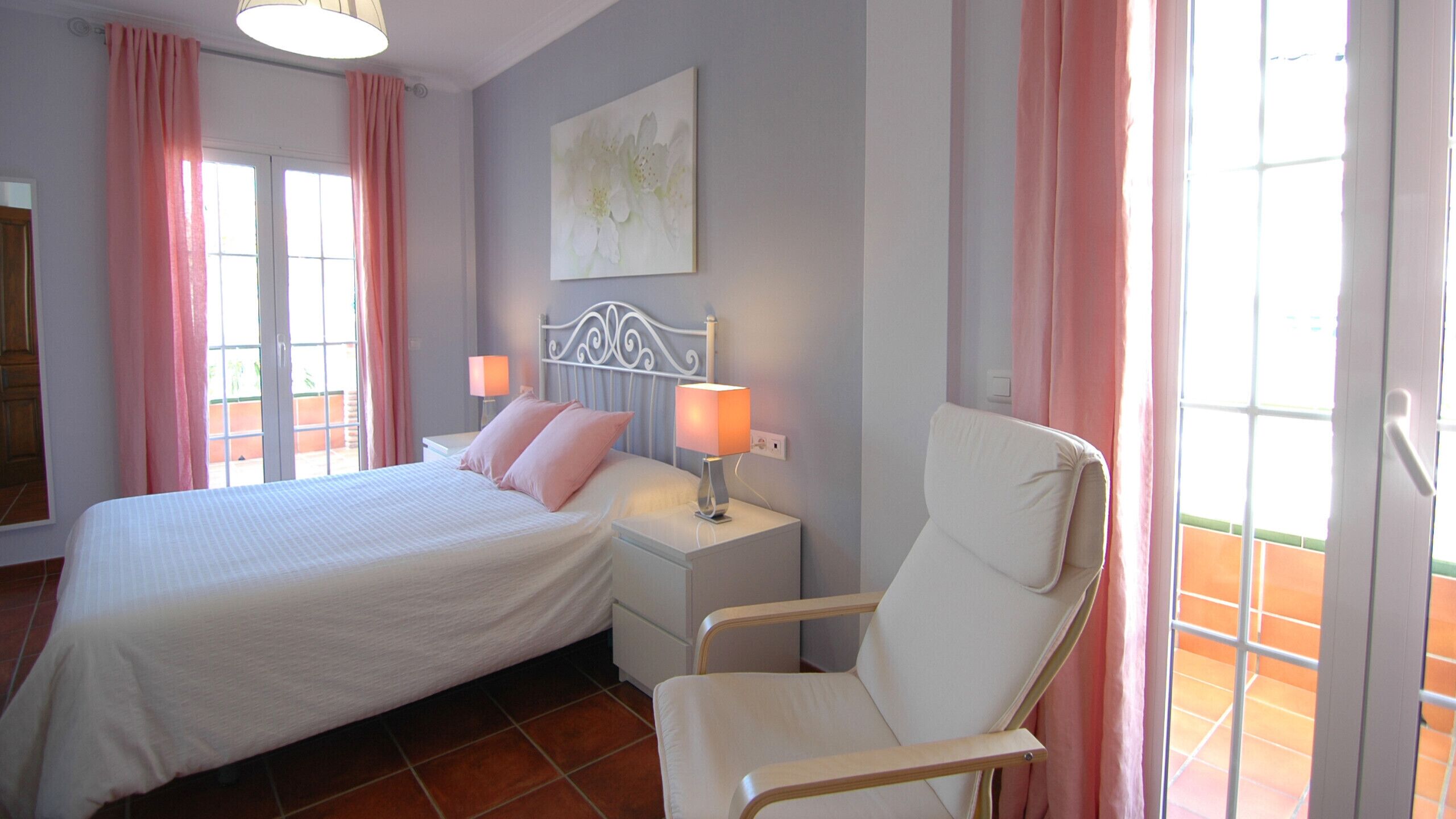 A bedroom with a bed, bedside lamps, a chair, and a window with curtains.