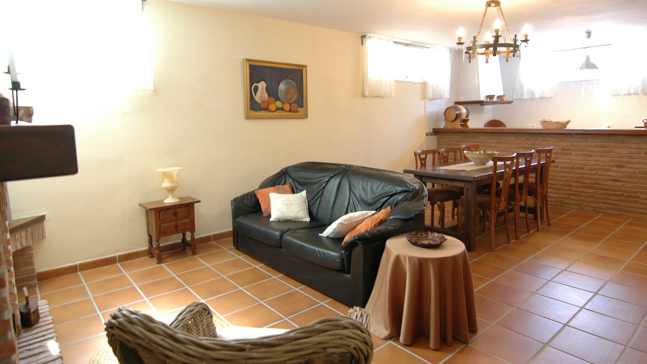 Un salon avec un canapé en cuir, une table à manger avec des chaises, un coin cuisine et un sol carrelé.