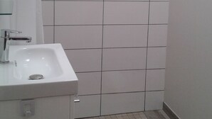 Un baño con un lavamanos blanco, un espejo y una pared de ducha con azulejos.